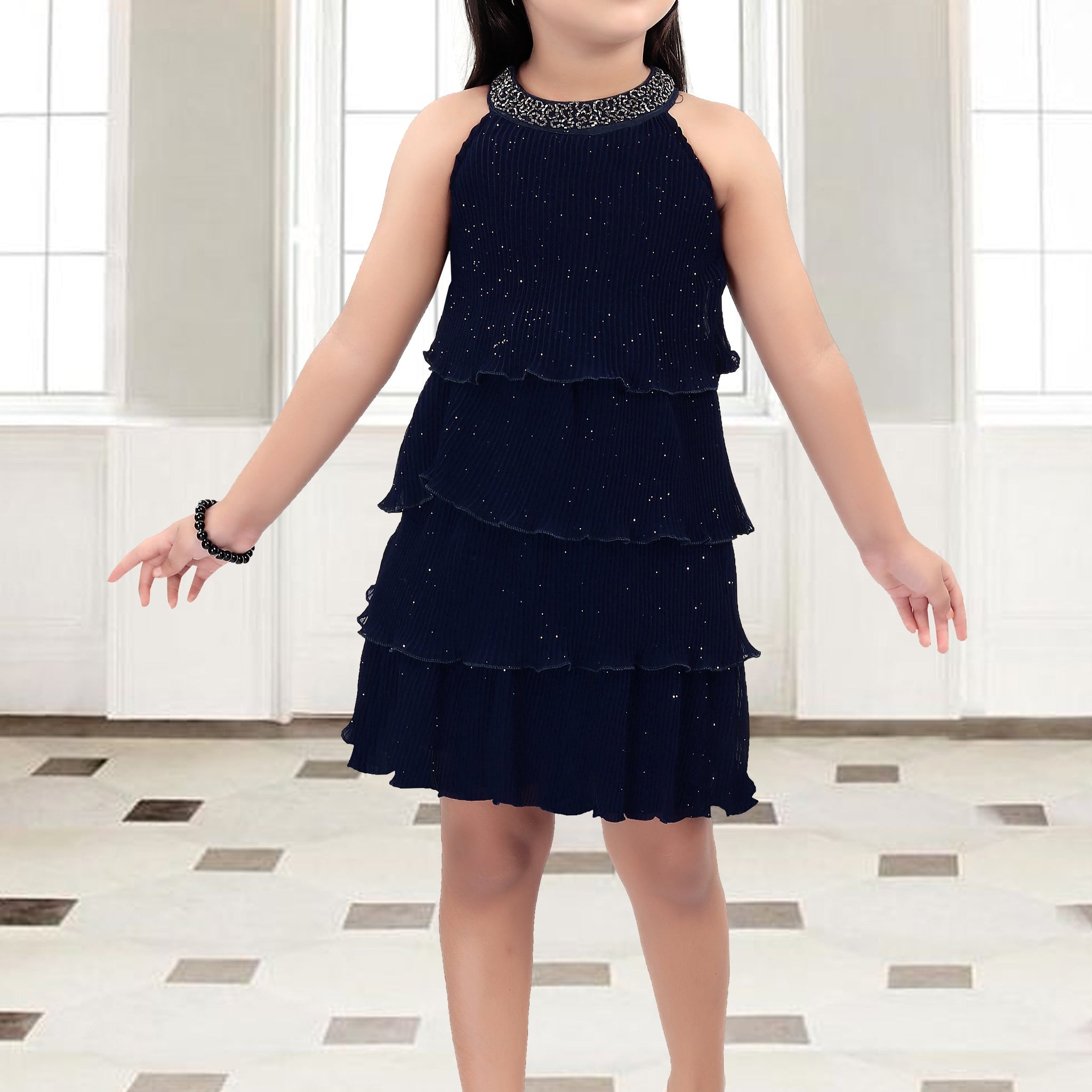 Young girl wearing a black tiered dress with a sparkly neckline in a room.