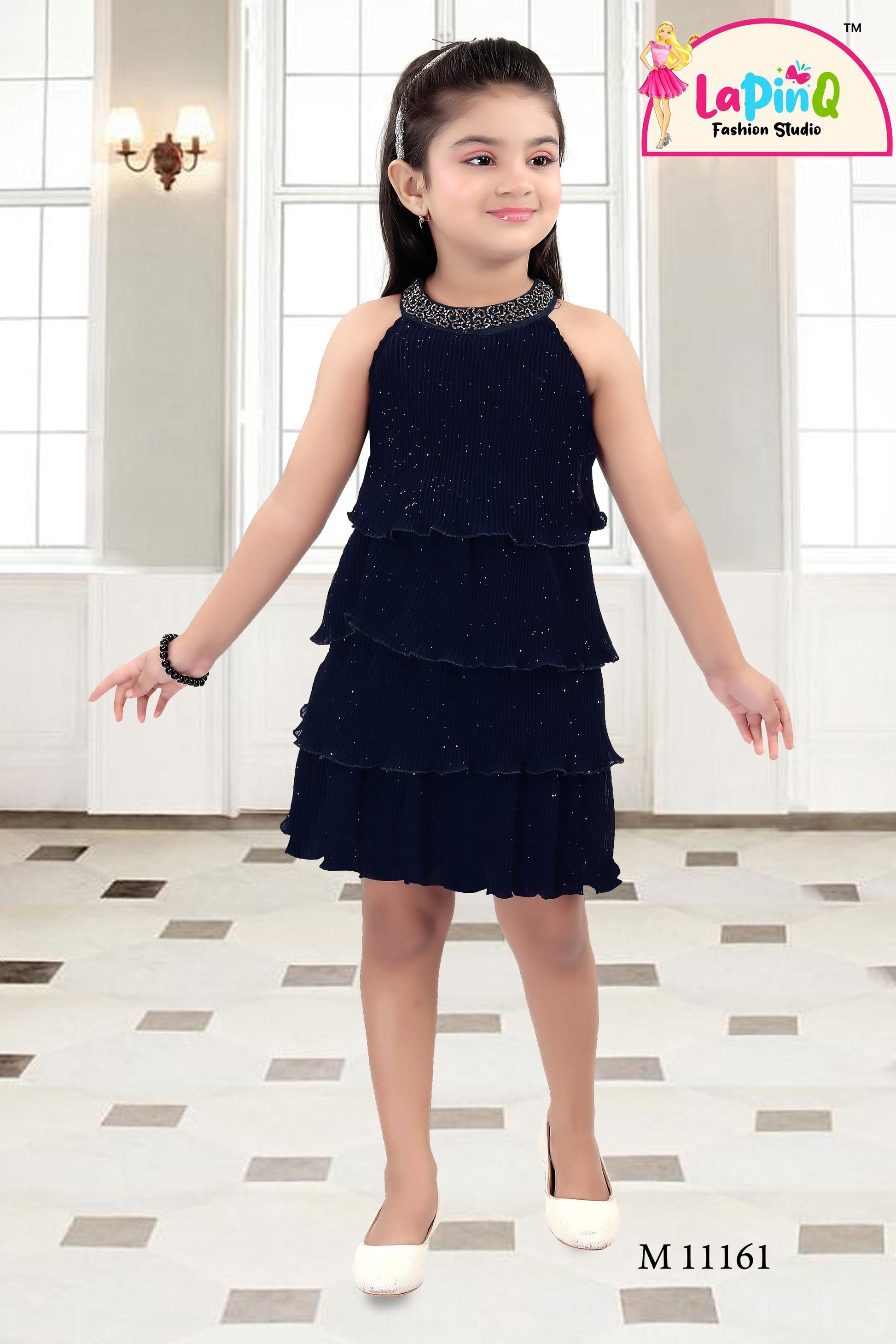 Young girl wearing a black tiered dress with a sparkly neckline in a room.